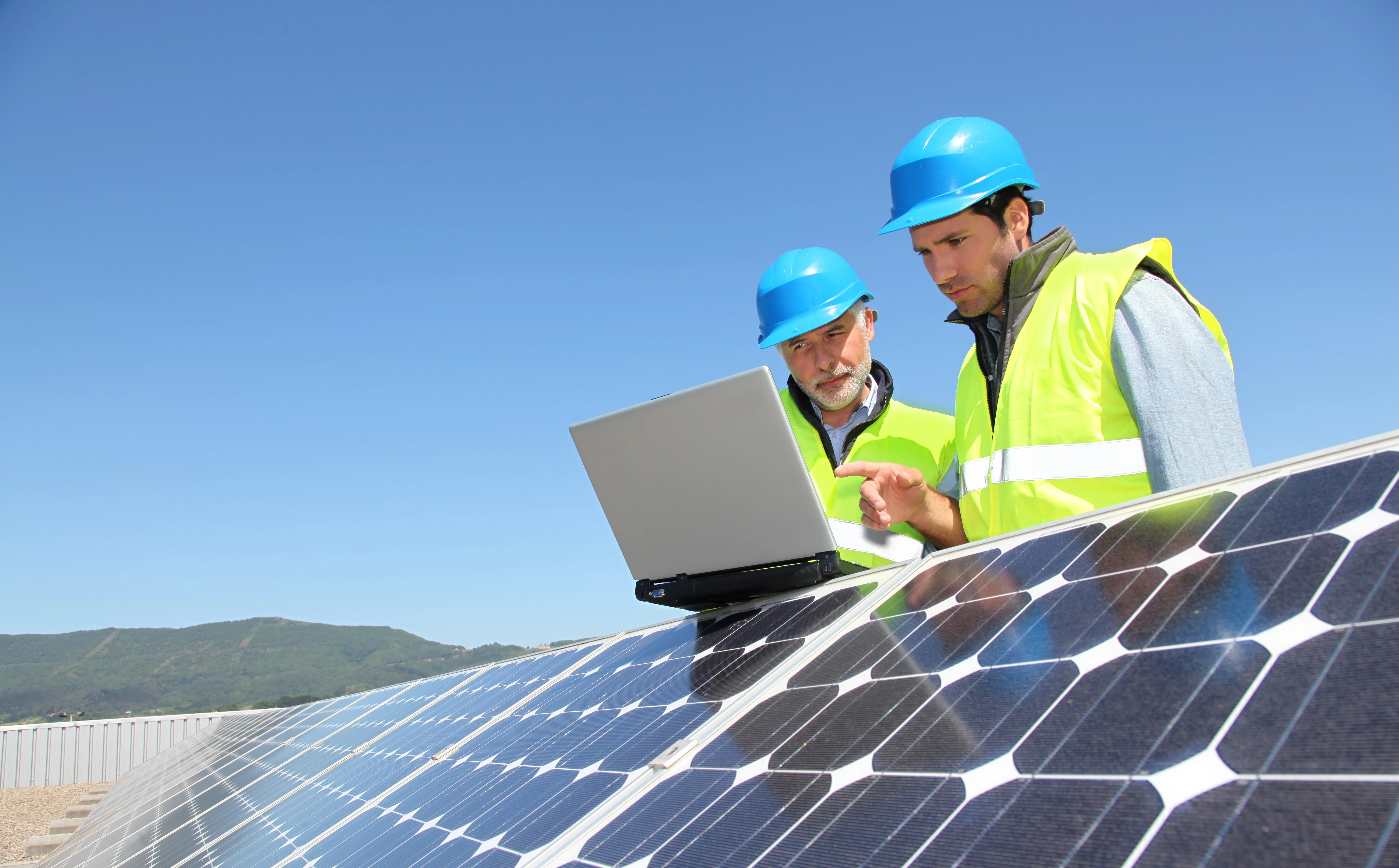 Two engineers in hard hats reviewing a laptop on a solar farm